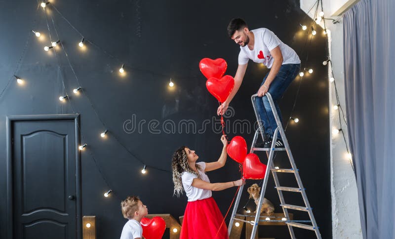 Préparation pour le jour du ` s de St Valentine La jeune famille accroche les ballons rouges de fête de coeur photos stock Préparation pour le jour du ` s de St Valentine La jeune famille accroche les ballons rouges de fête de coeur photos stock