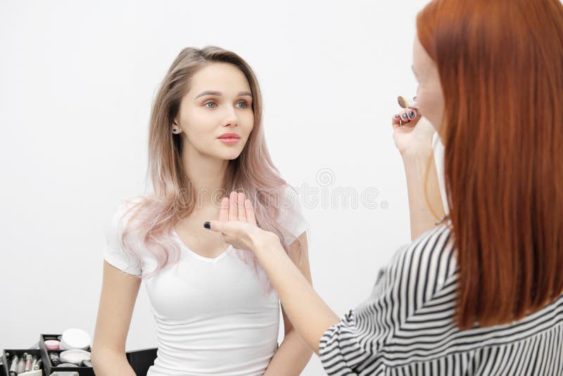 Préparez l'artiste la fille que rousse fait à maquillage le beau modèle blond de femme sur le fond blanc À côté du chariot avec d images libres de droits Préparez l'artiste la fille que rousse fait à maquillage le beau modèle blond de femme sur le fond blanc À côté du chariot avec d images libres de droits