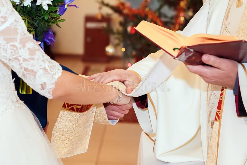 Prêtre tenant la main d'une mariée élégante et d'un marié élégant lors d'une cérémonie de mariage catholique à l'église