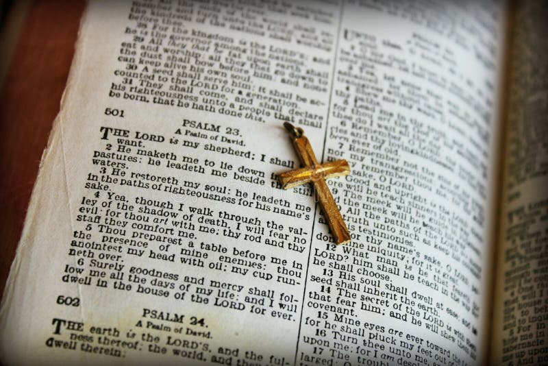 A vintage Bible opened to the 23rd Psalms with a golden cross. A vintage Bible opened to the 23rd Psalms with a golden cross.
