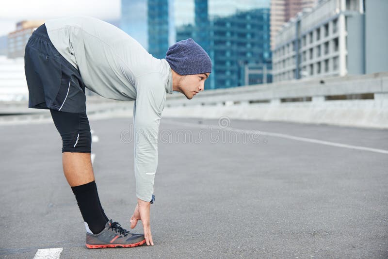 Psyching himself up for a run. a young man stretching before a jog through the quiet city streets. Psyching himself up for a run. a young man stretching before