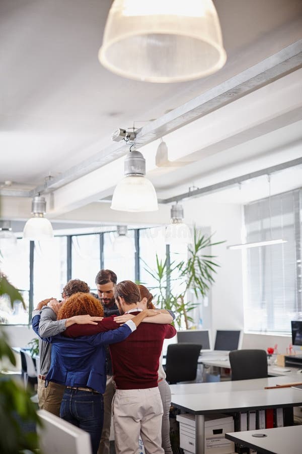 Psyching themselves up for the next challenge. a team of businesspeople forming a huddle in the middle of their office.