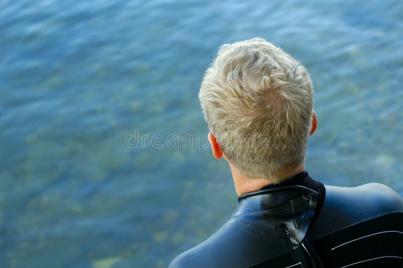 A triathlon swimmer, dressed in a wet suit, psyching himself up to go as he gazes at the cold clear water. A triathlon swimmer, dressed in a wet suit, psyching himself up to go as he gazes at the cold clear water.