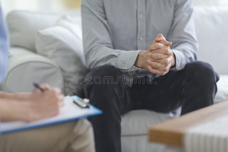 Psychologist taking notes during psychotherapy session with man