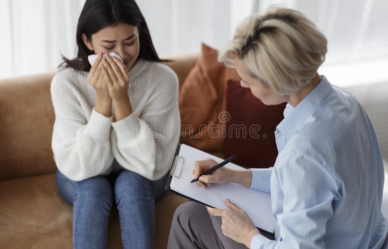 Psychotherapist taking notes listening to crying woman client during therapy session sitting on sofa in office. Selective focus. Therapist taking notes stock images, royalty-free photos and pictures