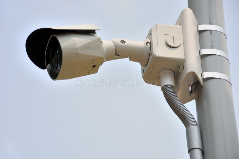A public surveillance camera installed on a lamp post against a light hazy cloudless blue sky