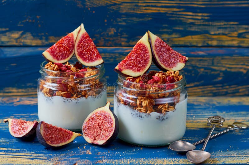 Pudim do leite de Chia com granola e os figos cortados frescos nos frascos de vidro na mesa de cozinha de madeira azul Café da ma imagem de stock royalty free Pudim do leite de Chia com granola e os figos cortados frescos nos frascos de vidro na mesa de cozinha de madeira azul Café da ma imagem de stock royalty free