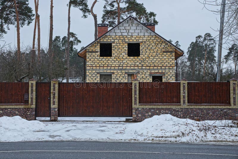 Puerta de Brown y cerca de madera delante de un hogar inacabado en la carretera de asfalto en la nieve fotos de archivo libres de regalías Puerta de Brown y cerca de madera delante de un hogar inacabado en la carretera de asfalto en la nieve fotos de archivo libres de regalías