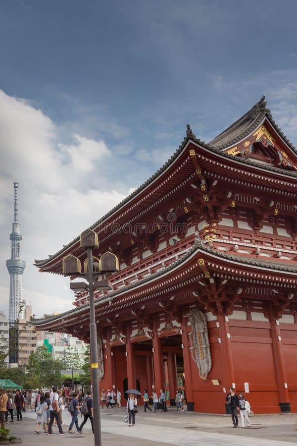 Tokyo, Japan - September 26, 2016: Vermilion and gold painted Hozomon Gate at Senso-ji Buddhist Temple with tall Skytree tower in the distance under blue cloudy sky. Lots of people. Blue cloudy sky. Tokyo, Japan - September 26, 2016: Vermilion and gold painted Hozomon Gate at Senso-ji Buddhist Temple with tall Skytree tower in the distance under blue cloudy sky. Lots of people. Blue cloudy sky.