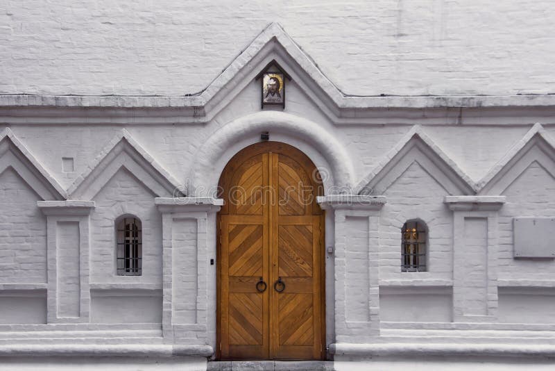 Puerta de madera y dos ventanas arqueadas en una pared de ladrillo blanca Entrada a la iglesia cristiana vieja imágenes de archivo libres de regalías Puerta de madera y dos ventanas arqueadas en una pared de ladrillo blanca Entrada a la iglesia cristiana vieja imágenes de archivo libres de regalías
