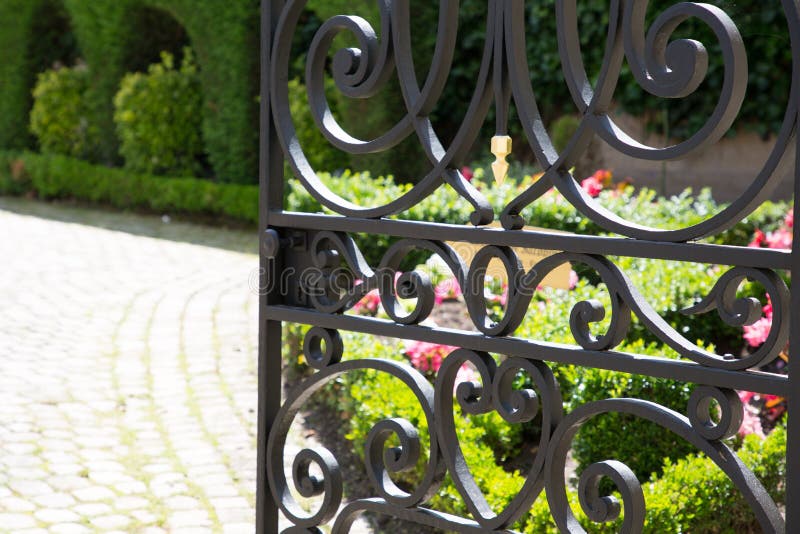 Puerta del hierro labrado abierta al jardín y a su calzada de la losa imagenes de archivo Puerta del hierro labrado abierta al jardín y a su calzada de la losa imagenes de archivo
