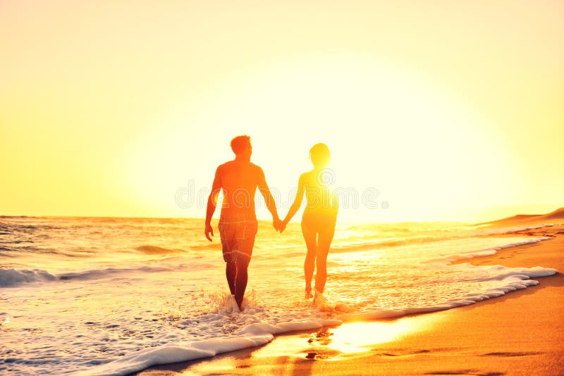 Puesta del sol romántica de las manos de los pares de la playa del verano que se sostiene