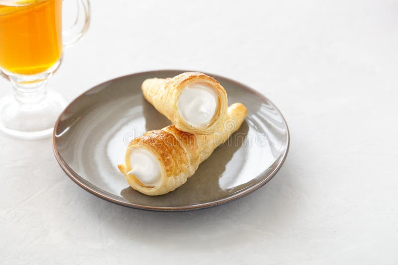 Puff pastry horn with white cream. Fresh dessert roll with cream or meringue and tea with lemon on a light background