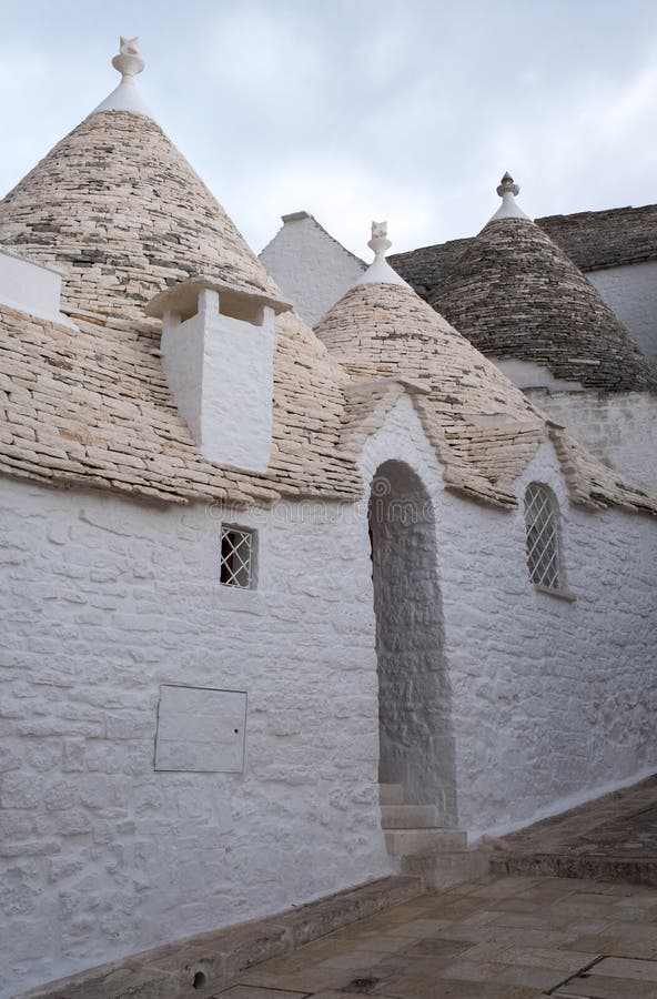 Puglia, Italië De traditionele droge steen kegel roofed trullihuizen achter poort op een straat in Alberobello royalty-vrije stock foto Puglia, Italië De traditionele droge steen kegel roofed trullihuizen achter poort op een straat in Alberobello royalty-vrije stock foto