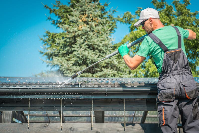 Roof and Gutters Power Cleaning Using Pressure Washer. Caucasian Worker. Roof and Gutters Power Cleaning Using Pressure Washer. Caucasian Worker.