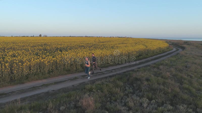 Pulsez dehors, de jeunes sports homme et course de femme le long de route près du pré de floraison de graine de colza pendant la