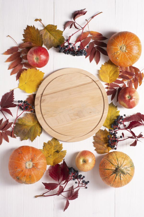 Pumpkin, apples, dry leaves, wild grapes lie on a white wooden background around a round board. Autumn composition. Autumn, fall