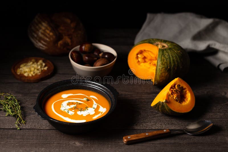 Pumpkin and chestnut soup with cream and thyme aside an open pumpkin, chestnuts and bread on a vintage dark wood background royalty free stock photos Pumpkin and chestnut soup with cream and thyme aside an open pumpkin, chestnuts and bread on a vintage dark wood background royalty free stock photos