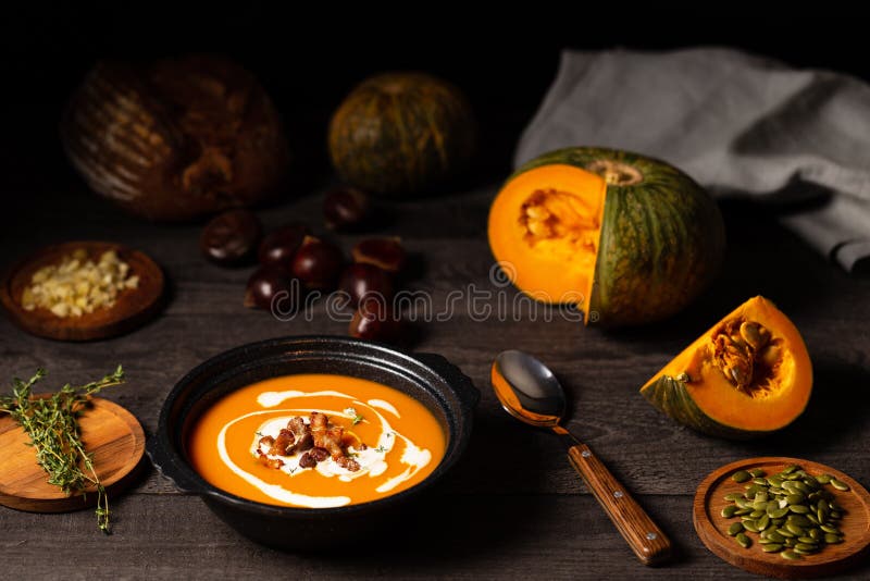 Pumpkin and chestnut soup with cream, pork belly and thyme aside an open pumpkin, chestnuts and bread on dark wood royalty free stock photo Pumpkin and chestnut soup with cream, pork belly and thyme aside an open pumpkin, chestnuts and bread on dark wood royalty free stock photo