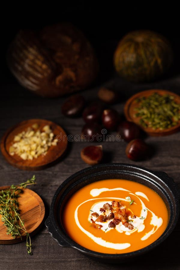 Pumpkin and chestnut soup with cream, pork belly and thyme aside seeds and thyme, chestnuts and bread on dark wood royalty free stock images Pumpkin and chestnut soup with cream, pork belly and thyme aside seeds and thyme, chestnuts and bread on dark wood royalty free stock images