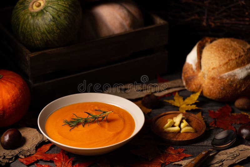 Pumpkin and chestnut soup with rosemary twig aside pumpkins, bread and chestnuts on a dark wood background spread with leaves stock photos Pumpkin and chestnut soup with rosemary twig aside pumpkins, bread and chestnuts on a dark wood background spread with leaves stock photos
