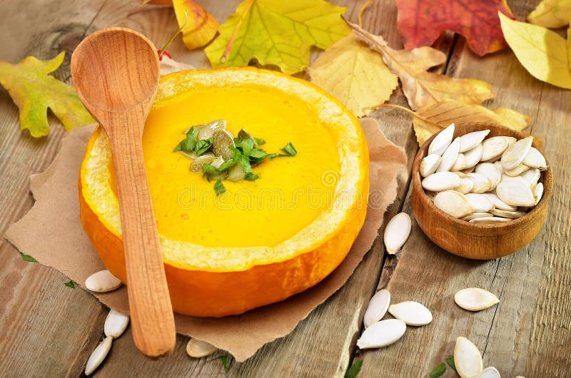 Pumpkin cream soup on rustic wooden table. Pumpkin cream soup, seeds and dry autumn leaves on rustic wooden table stock photography