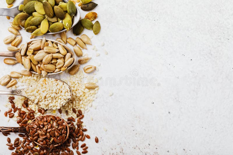 Pumpkin, flax, sesame and sunflower seeds in metal spoons on the left side of the table with copy space