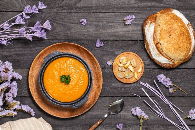 Pumpkin soup in black soup tureen aside chestnuts, bread and napkin on a dark wood background with purple dried flowers stock photos Pumpkin soup in black soup tureen aside chestnuts, bread and napkin on a dark wood background with purple dried flowers stock photos