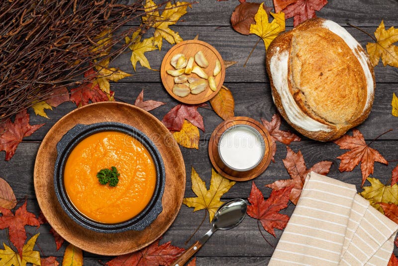 Pumpkin soup in black soup tureen aside chestnuts, cream, bread and napkin on a dark wood background with leaves and branches. royalty free stock images Pumpkin soup in black soup tureen aside chestnuts, cream, bread and napkin on a dark wood background with leaves and branches. royalty free stock images