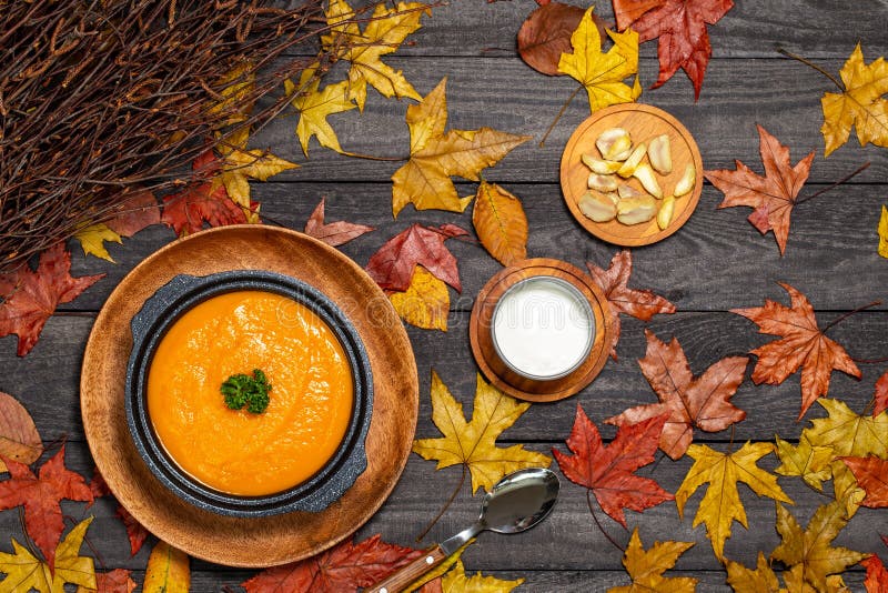 Pumpkin soup in black soup tureen aside chestnuts and cream on a dark wood background with leaves and branches. Flat Lay. royalty free stock images Pumpkin soup in black soup tureen aside chestnuts and cream on a dark wood background with leaves and branches. Flat Lay. royalty free stock images