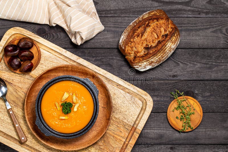 Pumpkin soup in black soup tureen aside entire chestnuts all on a board on a dark wood background with thyme twigs. Flat Lay royalty free stock photos Pumpkin soup in black soup tureen aside entire chestnuts all on a board on a dark wood background with thyme twigs. Flat Lay royalty free stock photos