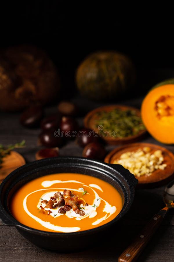 Pumpkin soup with cream, pork belly and thyme aside seeds and thyme, chestnuts and bread on a vintage dark wood background. royalty free stock photography Pumpkin soup with cream, pork belly and thyme aside seeds and thyme, chestnuts and bread on a vintage dark wood background. royalty free stock photography