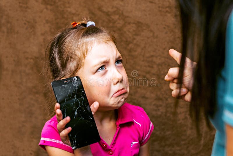 Punishment of a child for a spoiled mobile phone. Little girl cries and apologizes. Mom scolds her daughter for a broken phone. A