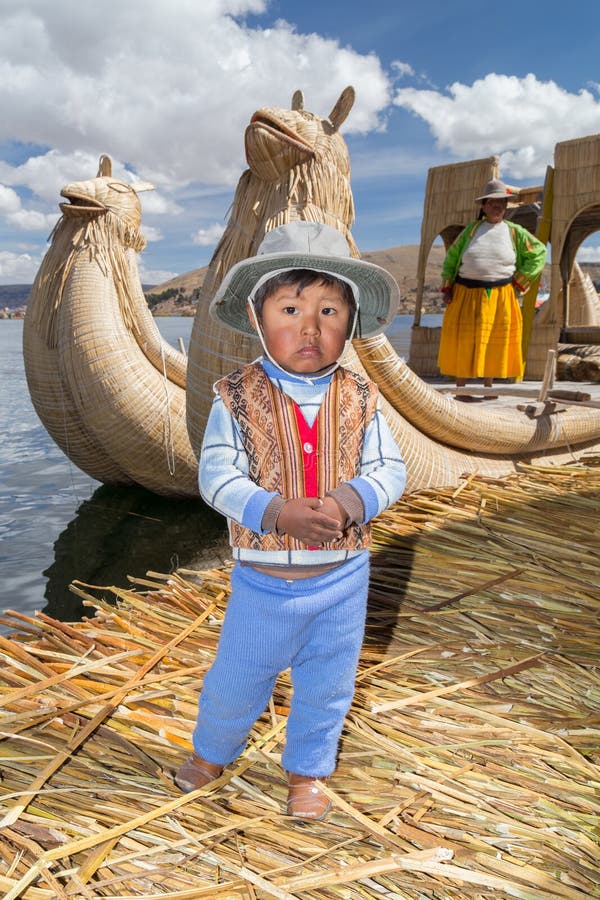 Puno, Peru - około Czerwiec 2015: Mała chłopiec w tradycyjnych ubraniach i kajakowej łodzi przy Uros spławową wyspą wioską na Jez obraz royalty free