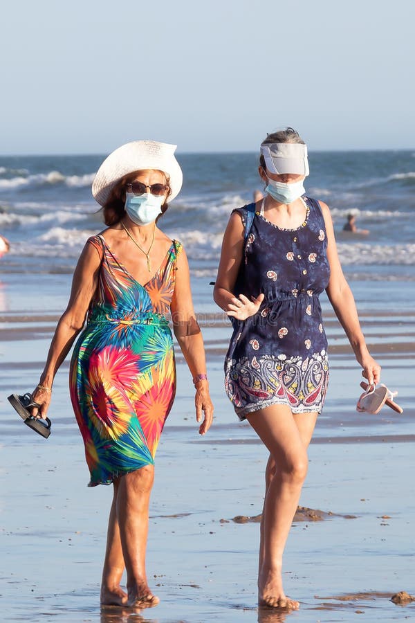 Punta Umbria, Huelva, Spain - August 2, 2020: Two women walking by the beach wearing protective or medical face masks. New normal