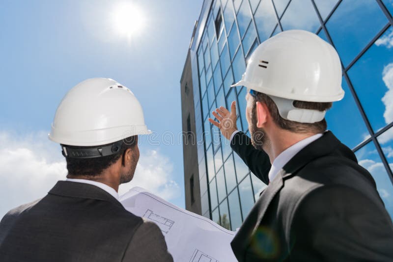 Punto di vista di angolo basso degli architetti professionisti nel lavoro degli elmetti protettivi fotografia stock Punto di vista di angolo basso degli architetti professionisti nel lavoro degli elmetti protettivi fotografia stock