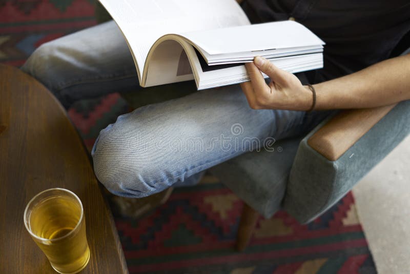 Punto di vista del primo piano di una tenuta della mano dell'uomo che legge rivista di moda moderna, vetro di birra in caffè immagine stock Punto di vista del primo piano di una tenuta della mano dell'uomo che legge rivista di moda moderna, vetro di birra in caffè immagine stock