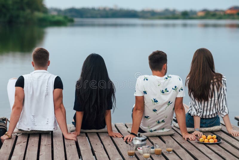 Punto di vista posteriore degli amici che si rilassano sul pilastro del fiume fotografia stock libera da diritti Punto di vista posteriore degli amici che si rilassano sul pilastro del fiume fotografia stock libera da diritti