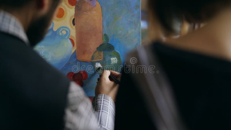 Back view of Skilled artist men teaching and showing young women the basics of painting in art studio. Back view of Skilled artist men teaching and showing young women the basics of painting in art studio