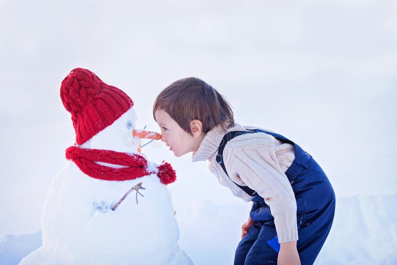 Pupazzo di neve felice della costruzione del bello bambino in giardino, inverno, naso t fotografia stock libera da diritti Pupazzo di neve felice della costruzione del bello bambino in giardino, inverno, naso t fotografia stock libera da diritti