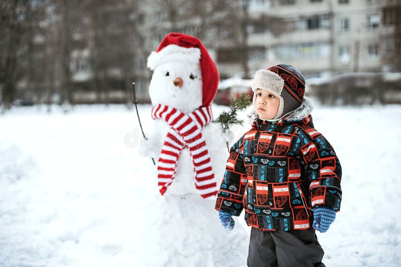 Pupazzo di neve felice della costruzione del bello bambino in giardino, orario invernale, immagini stock libere da diritti Pupazzo di neve felice della costruzione del bello bambino in giardino, orario invernale, immagini stock libere da diritti