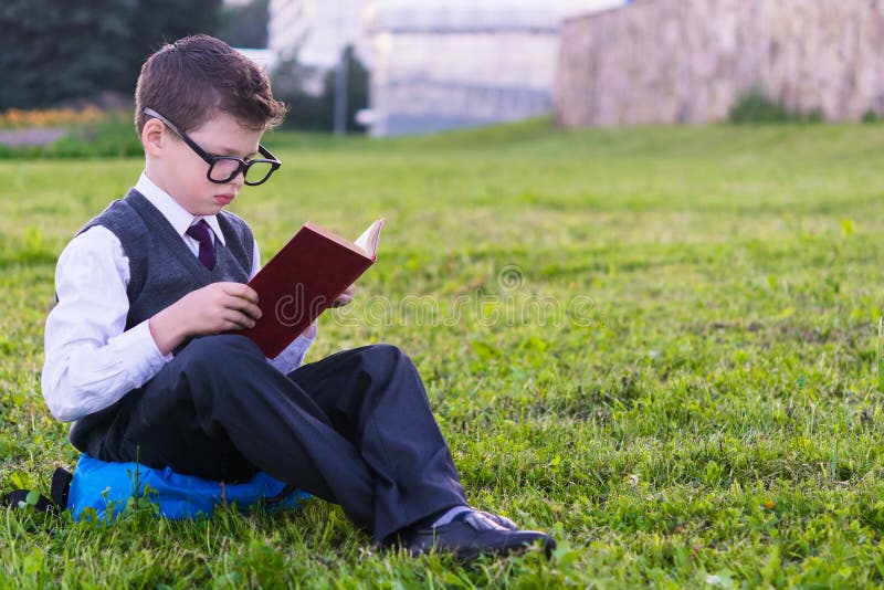 Pupil in glasses reads a book sitting on the grass royalty free stock image Pupil in glasses reads a book sitting on the grass royalty free stock image