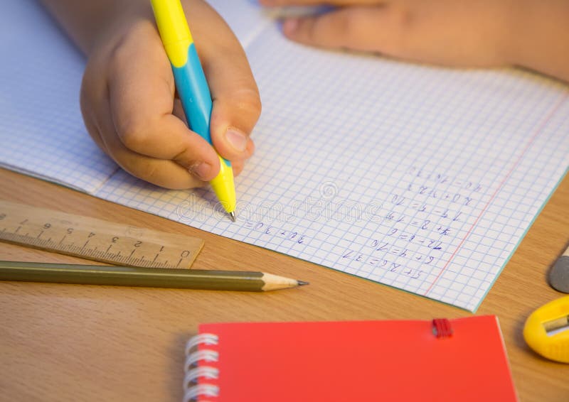 Pupil s hand close-up solves math examples with a ballpoint pen. A schoolboy performs a task at the workplace. The concept of children s education, teaching knowledge, skills and abilities.