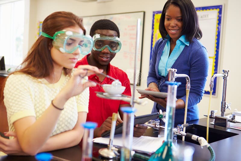 Gli Alunni Lo Svolgimento Dell'Esperimento In Classe Di Scienza Indossare Occhiali Di Sicurezza Con L'Insegnante Di Guardare.