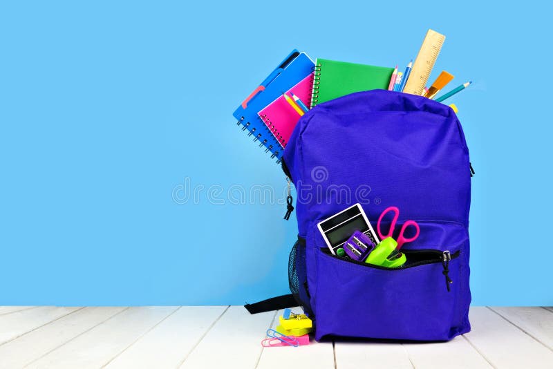 Purple backpack full of school supplies against a blue background. Back to school. stock photo