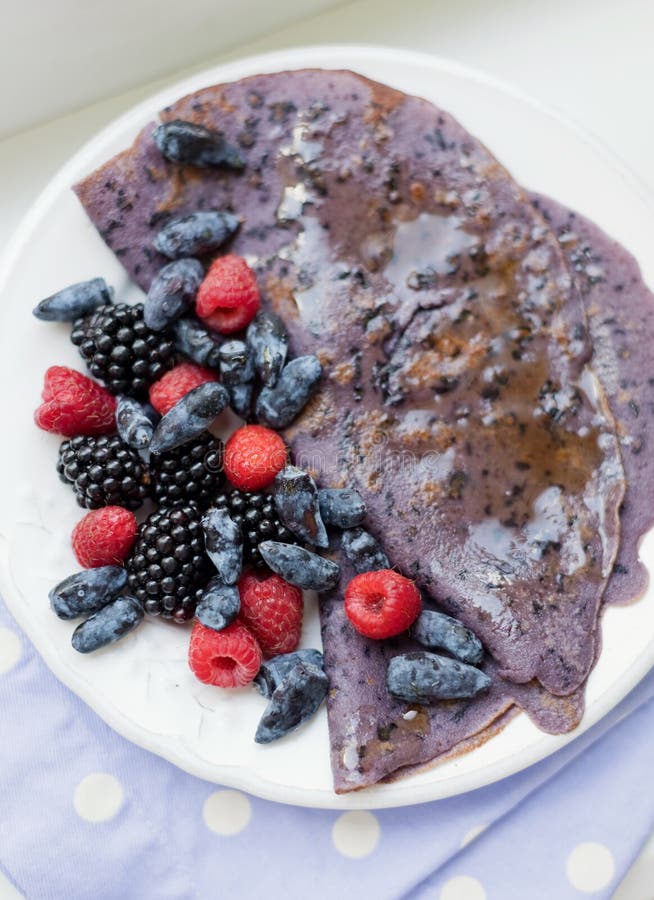 Purple crepes with berries and syrup