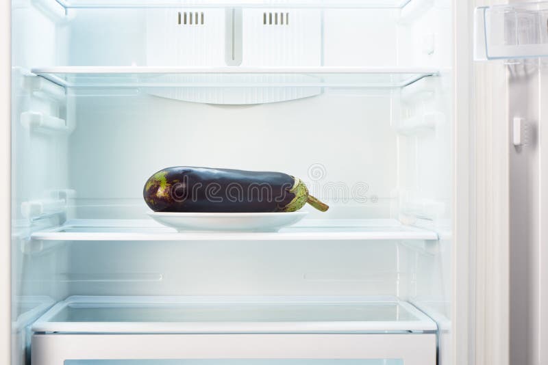 Purple Eggplant on White Plate in Open Empty Refrigerator Stock Photo