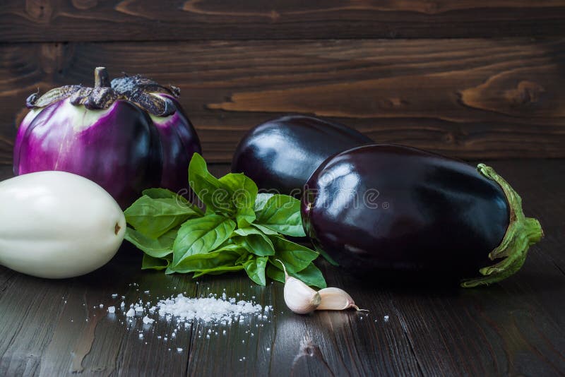 Purple and white eggplant (aubergine) with basil on dark wooden table. Fresh raw farm vegetables - harvest from the gard stock photos Purple and white eggplant (aubergine) with basil on dark wooden table. Fresh raw farm vegetables - harvest from the gard stock photos
