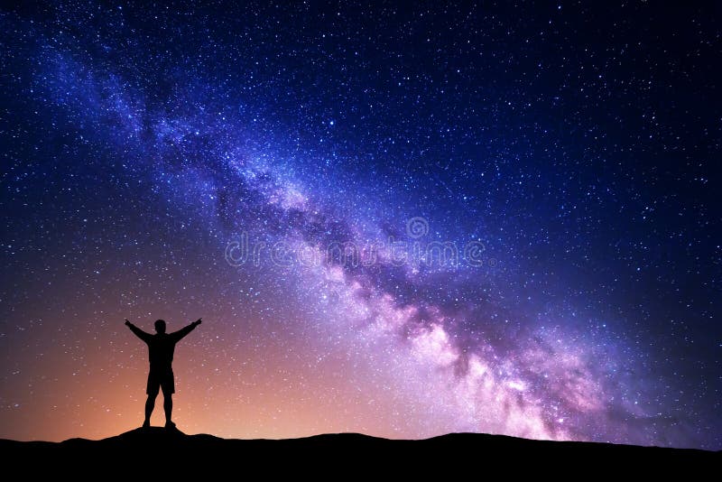 Purple Milky Way with silhouette of a standing man with raised up arms on the hill. Night landscape with beautiful galaxy. Universe. Night starry sky with Milky Way and yellow light. Purple Milky Way with silhouette of a standing man with raised up arms on the hill. Night landscape with beautiful galaxy. Universe. Night starry sky with Milky Way and yellow light