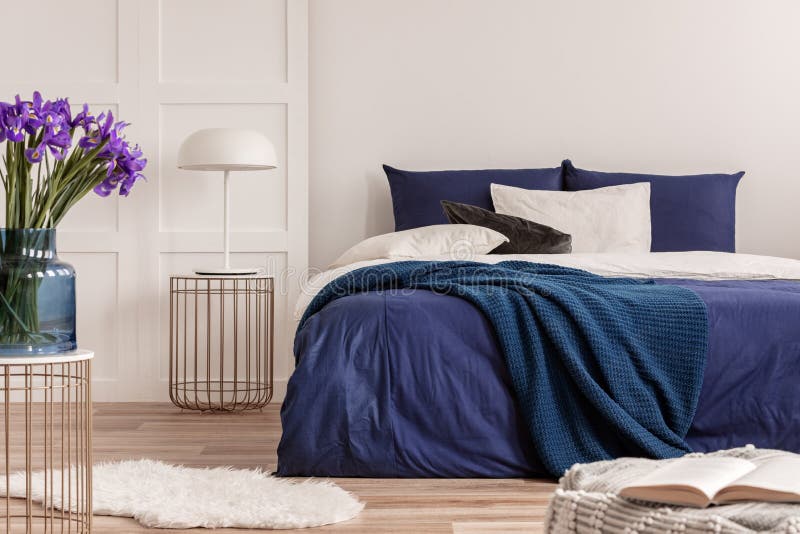 Purpurrote Blumen im blauen Glasvase auf stilvoller Tabelle im weißen Schlafzimmer Innen mit bequemem Bett lizenzfreie stockbilder Purpurrote Blumen im blauen Glasvase auf stilvoller Tabelle im weißen Schlafzimmer Innen mit bequemem Bett lizenzfreie stockbilder